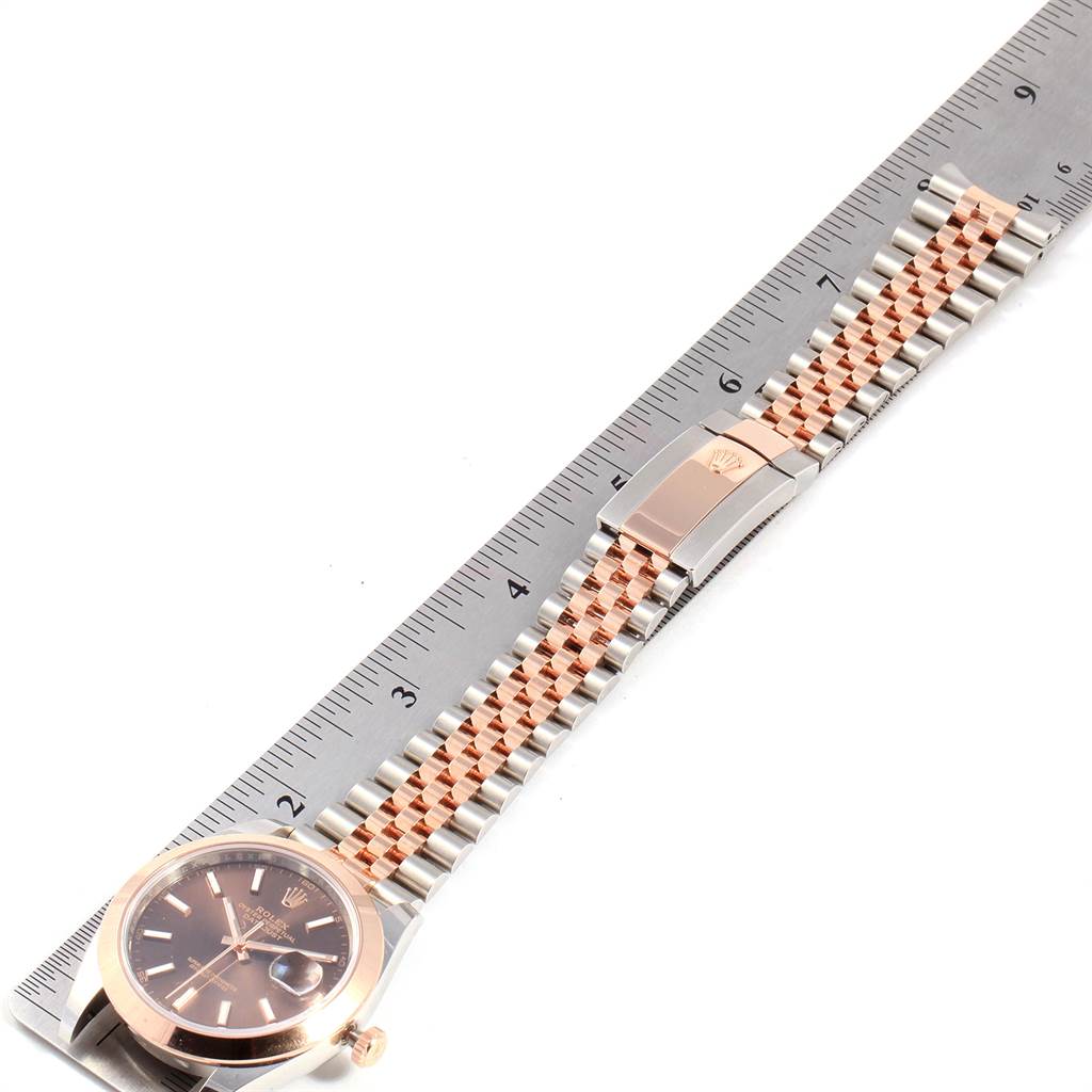 The Rolex Datejust 41 126301 Men's Steel and Gold (two tone) Brown Dial 126301 Men's Steel and Gold (two tone) Brown Dial model is shown from an overhead angle, displaying the face, bracelet, and clasp next to a ruler.