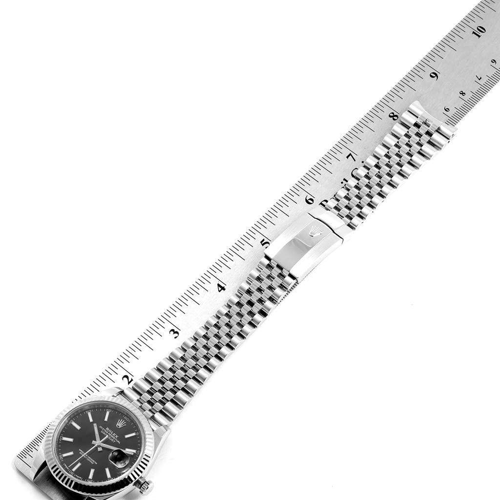 The Rolex Datejust 41 126334 Men's Stainless Steel Black Dial 126334 Men's Stainless Steel Black Dial watch is shown laid flat, alongside a ruler, highlighting its face and Jubilee bracelet.