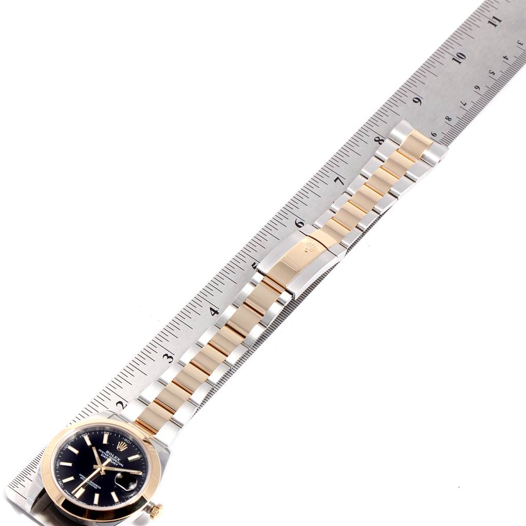 The Rolex Datejust 41 126303 Men's Steel and Gold (two tone) Black Dial 126303 Men's Steel and Gold (two tone) Black Dial watch is shown at an angle with a ruler, displaying the face and entire bracelet.
