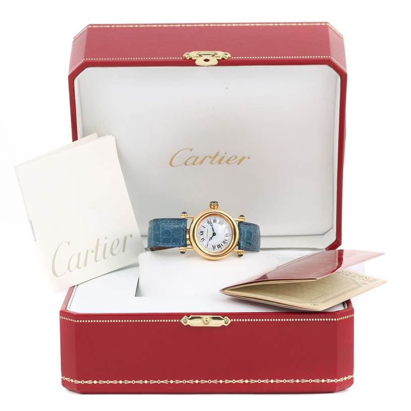 The image shows a Cartier Diabolo 1400 Women
s Yellow Gold Silver Dial 1400 Women
s Yellow Gold Silver Dial model watch with a blue strap in an open red Cartier box, along with booklets.