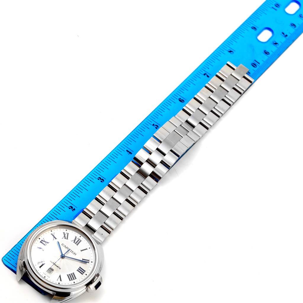 The Cartier Clé watch is shown from an overhead angle, featuring its face, metal bracelet, and a ruler for scale.