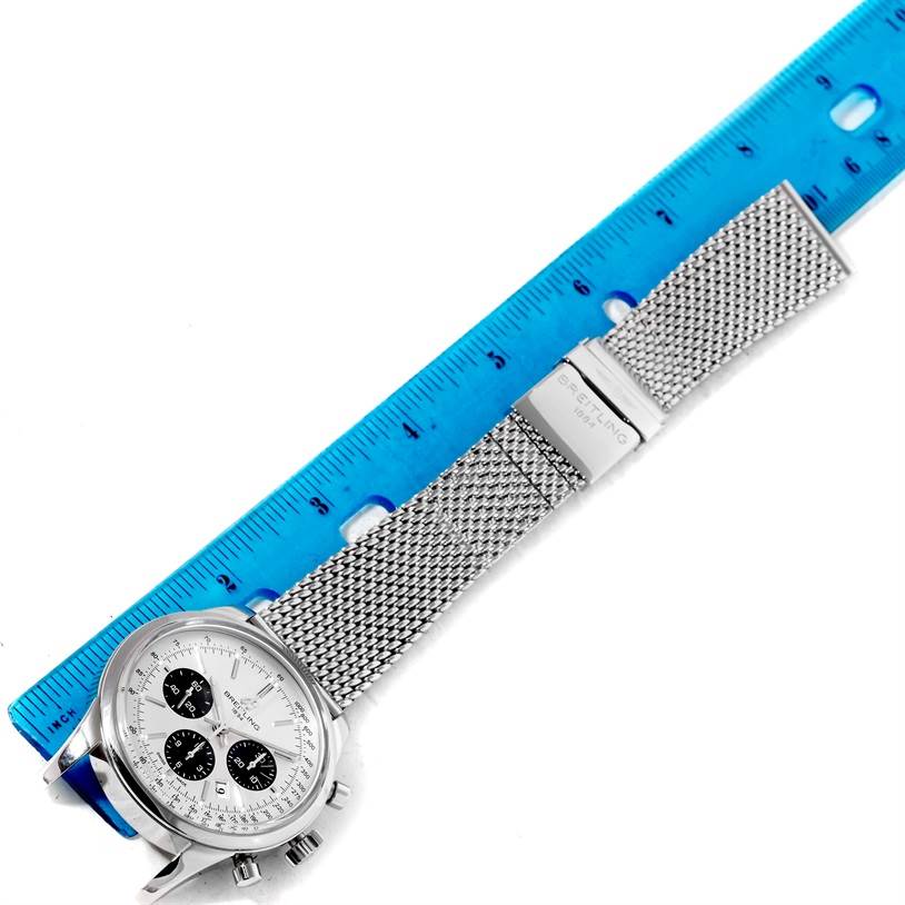 A Breitling Transocean AB015212/G724-154A Men
s Stainless Steel Silver Dial AB015212/G724-154A Men
s Stainless Steel Silver Dial watch is shown from a top-down angle with a metal mesh strap and clasp alongside a blue ruler.