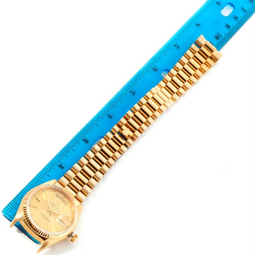 The image shows a gold Rolex President 18038 Men
s Yellow Gold Champagne Dial 18038 Men
s Yellow Gold Champagne Dial model watch laid flat next to a blue ruler.