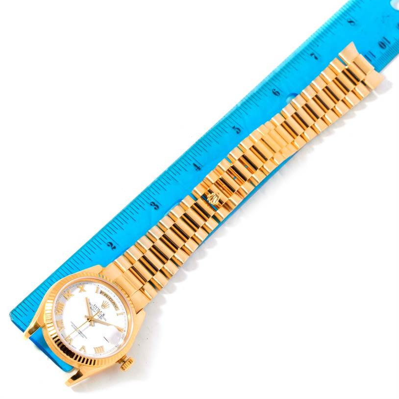 The Rolex President 118238 Men
s Yellow Gold White Dial 118238 Men
s Yellow Gold White Dial model watch is shown from a top-down angle, highlighting the face and the entire bracelet next to a blue ruler.