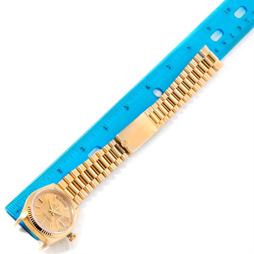 This image shows a gold Rolex President 18038 Men
s Yellow Gold Champagne Dial 18038 Men
s Yellow Gold Champagne Dial watch with its entire face, bracelet, and clasp, laid next to a blue ruler.