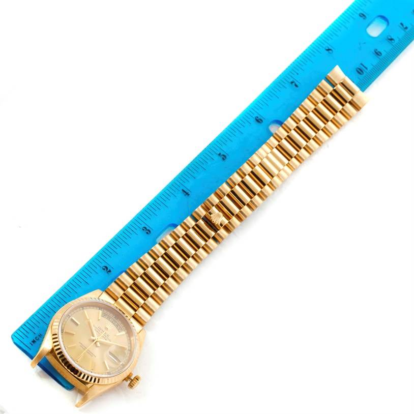 This image shows a Rolex President 18238 Men
s Yellow Gold Champagne Dial 18238 Men
s Yellow Gold Champagne Dial model watch laid next to a blue ruler for scale, displaying its face and bracelet.