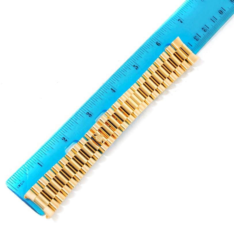 This image shows a gold bracelet of the Rolex President Men's  Men's  model watch alongside a blue measuring ruler.