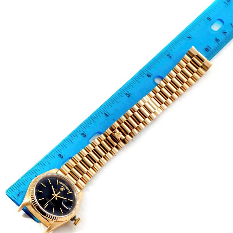 The Rolex President 18038 Men's Yellow Gold Black Dial 18038 Men's Yellow Gold Black Dial model watch is shown from the top view, displaying the face, bezel, and full bracelet alongside a ruler.