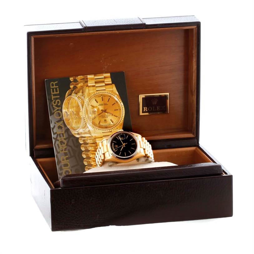 This photo shows a Rolex President 18038 Men's Yellow Gold Black Dial 18038 Men's Yellow Gold Black Dial model watch, displayed in its box with an accompanying booklet.