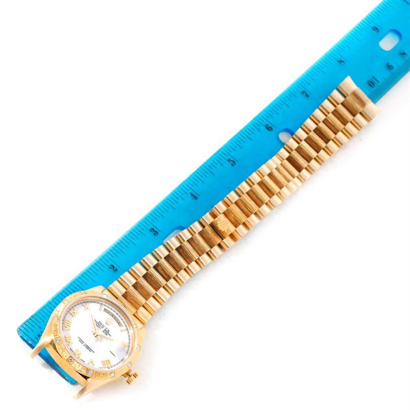 The image shows a top view of a Rolex President 18308 Men's Yellow Gold White Dial 18308 Men's Yellow Gold White Dial watch, featuring its face, case, and full bracelet placed beside a blue ruler.