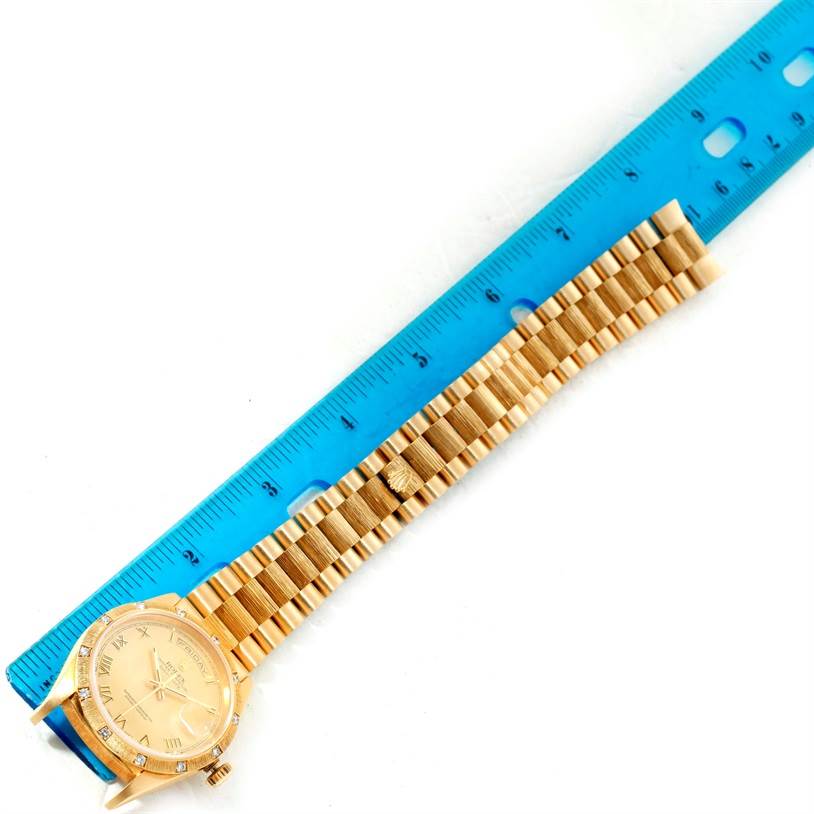 The image shows a Rolex President 18308 Men
s Yellow Gold Champagne Dial 18308 Men
s Yellow Gold Champagne Dial model watch placed next to a blue ruler, highlighting its gold watch face and bracelet.