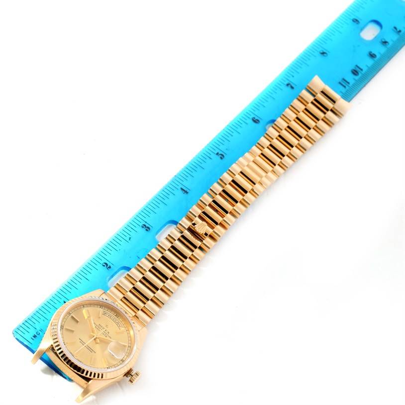 The image shows a Rolex President 18238 Men
s Yellow Gold Champagne Dial 18238 Men
s Yellow Gold Champagne Dial model watch laid flat next to a blue ruler, highlighting its full length and gold bracelet.