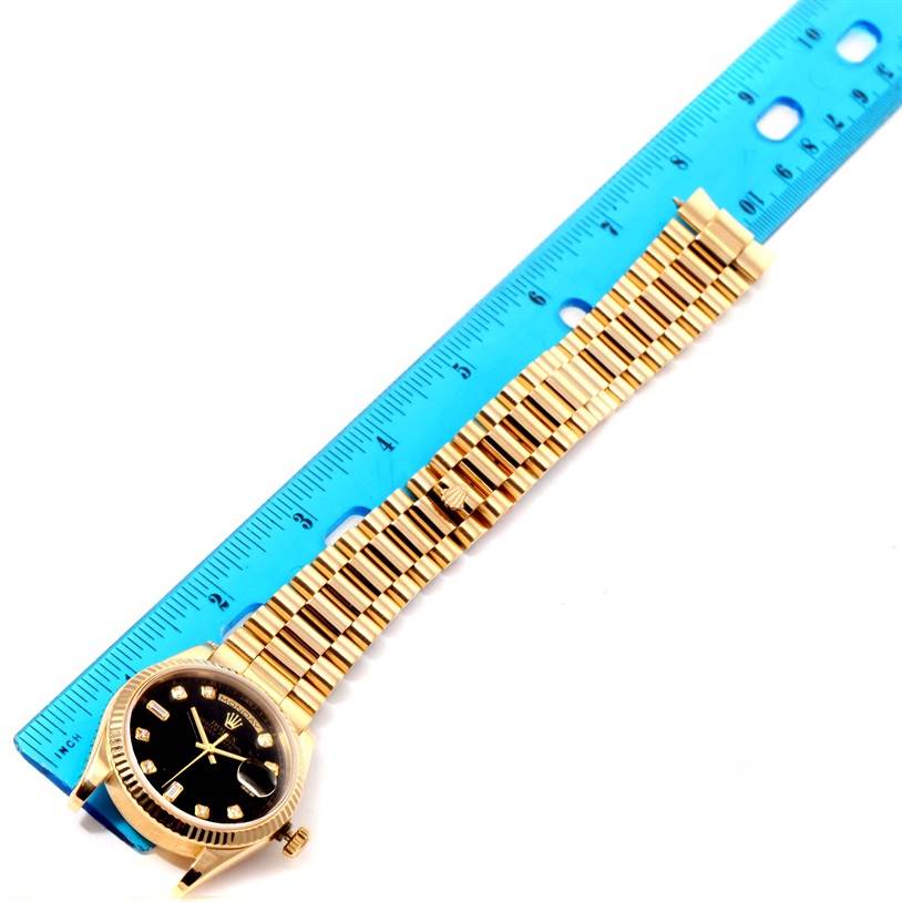 The image shows a Rolex President 118238 Men
s Yellow Gold Black Dial 118238 Men
s Yellow Gold Black Dial model watch from an overhead angle, including its face and band beside a blue ruler for scale.