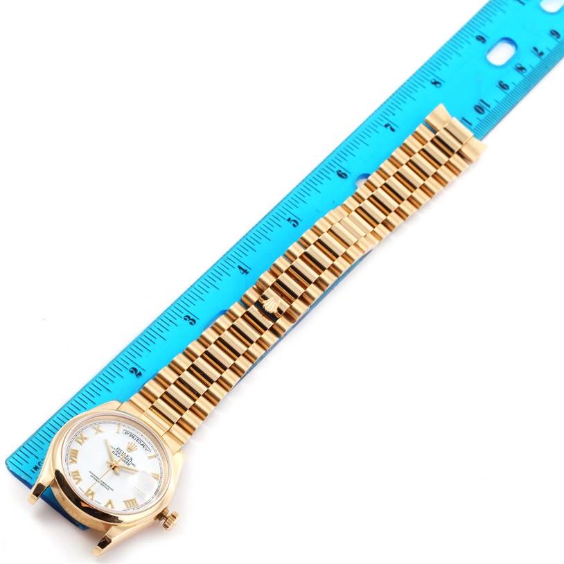 The image shows a top-down view of a Rolex President 118208 Men
s Yellow Gold White Dial 118208 Men
s Yellow Gold White Dial model watch with its band, next to a blue ruler for scale.