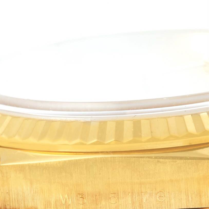 This close-up side view of the Rolex President 18238 Men
s Yellow Gold Champagne Dial 18238 Men
s Yellow Gold Champagne Dial model watch shows part of the fluted bezel, crystal, and case with serial number engraving.