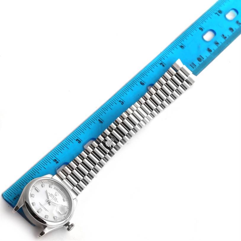 The Rolex President 118206 Men's Platinum Silver Dial 118206 Men's Platinum Silver Dial watch is shown from an overhead view with a blue ruler beside it, highlighting its band and dial.