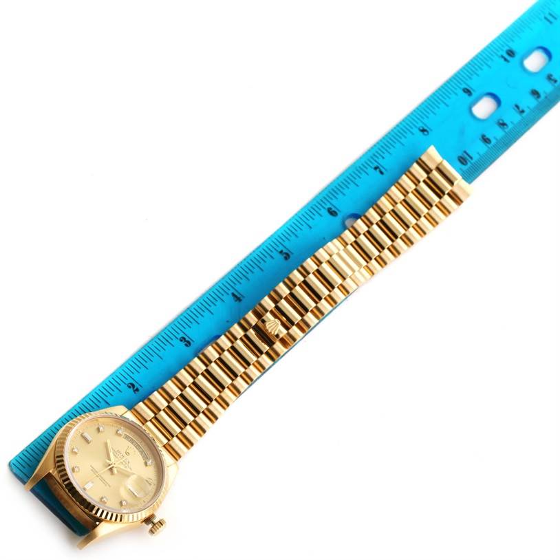 The image shows a Rolex President 18238 Men
s Yellow Gold Champagne Dial 18238 Men
s Yellow Gold Champagne Dial model watch lying flat, with a full view of the watch face and band, next to a blue ruler for scale.