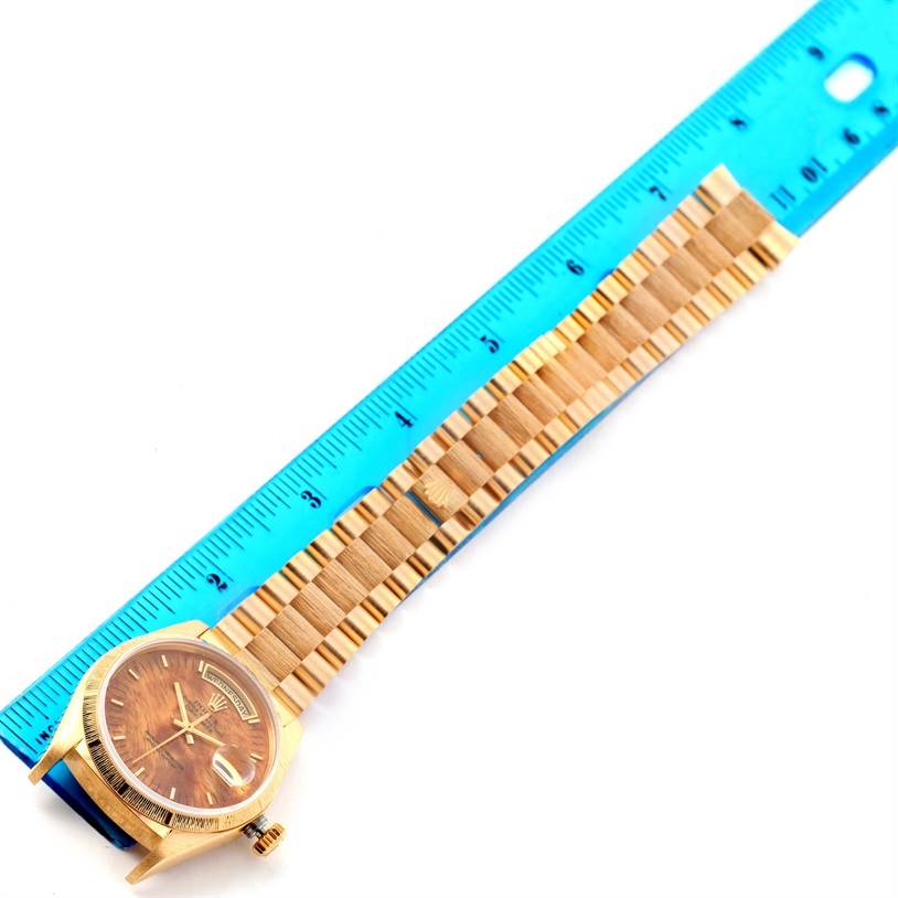 A Rolex President 18078 Men's Yellow Gold Brown Dial 18078 Men's Yellow Gold Brown Dial model watch is shown from a top-down angle alongside a blue ruler, displaying the case and bracelet.