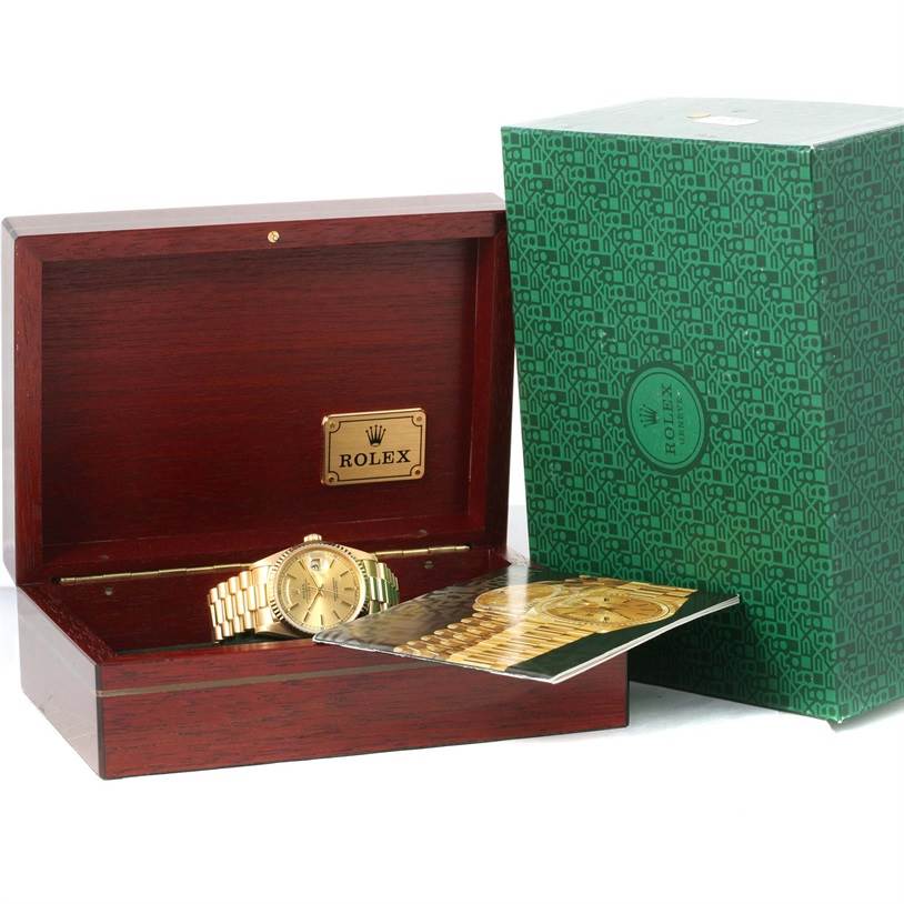 The image shows a Rolex President 18238 Men
s Yellow Gold Champagne Dial 18238 Men
s Yellow Gold Champagne Dial model watch in a wooden box, beside a green patterned box and a booklet.