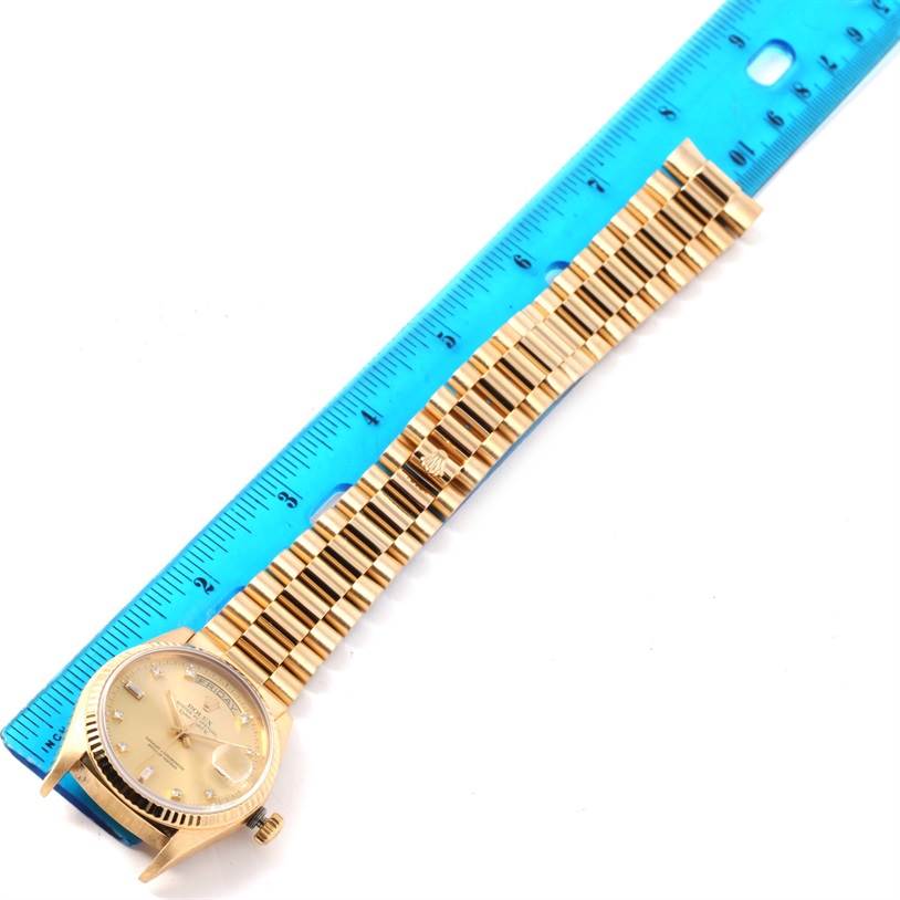 The image shows a Rolex President 18038 Men
s Yellow Gold Champagne Dial 18038 Men
s Yellow Gold Champagne Dial model watch lying flat with its face and bracelet visible, next to a blue ruler.