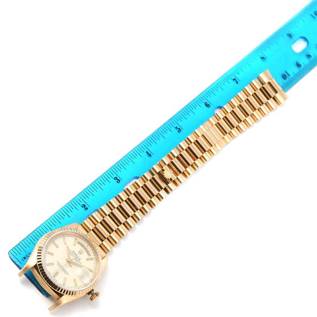 The Rolex President 18238 Men
s Yellow Gold Beige Dial 18238 Men
s Yellow Gold Beige Dial watch is shown laying flat next to a blue ruler, displaying the watch face and entire band.