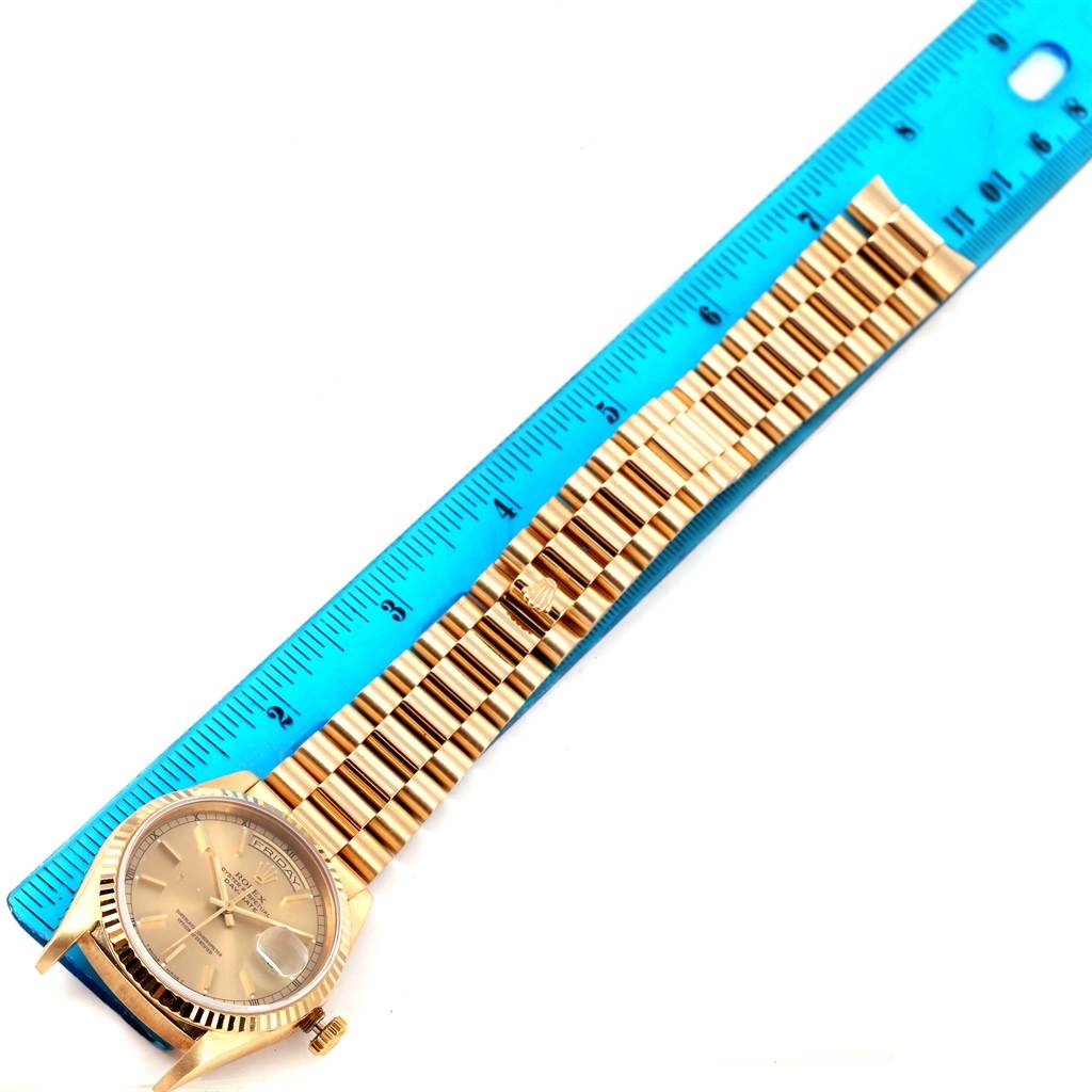 The image shows a Rolex President 18238 Men
s Yellow Gold Champagne Dial 18238 Men
s Yellow Gold Champagne Dial watch face and band placed next to a blue ruler.