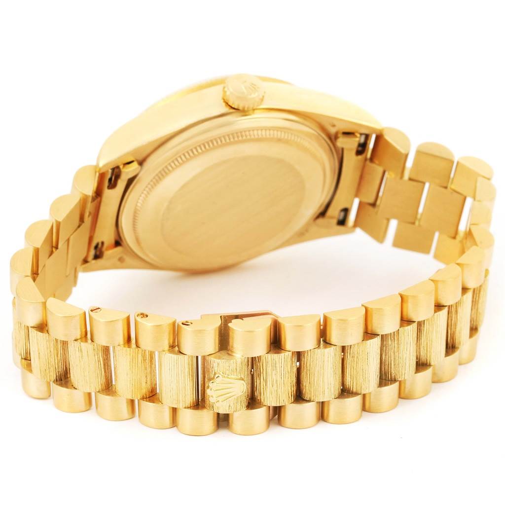 The image shows the back case and bracelet of a Rolex President 18078 Men
s Yellow Gold White Dial 18078 Men
s Yellow Gold White Dial model watch at an angle displaying the clasp logo.