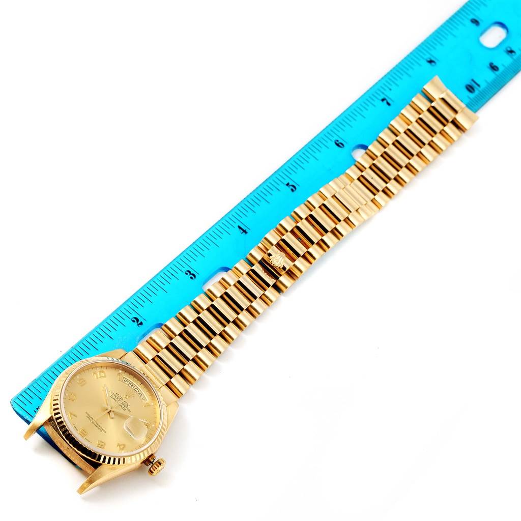 The image shows a Rolex President 18238 Men
s Yellow Gold Champagne Dial 18238 Men
s Yellow Gold Champagne Dial model watch and its gold bracelet laid next to a blue ruler, displaying the full length.