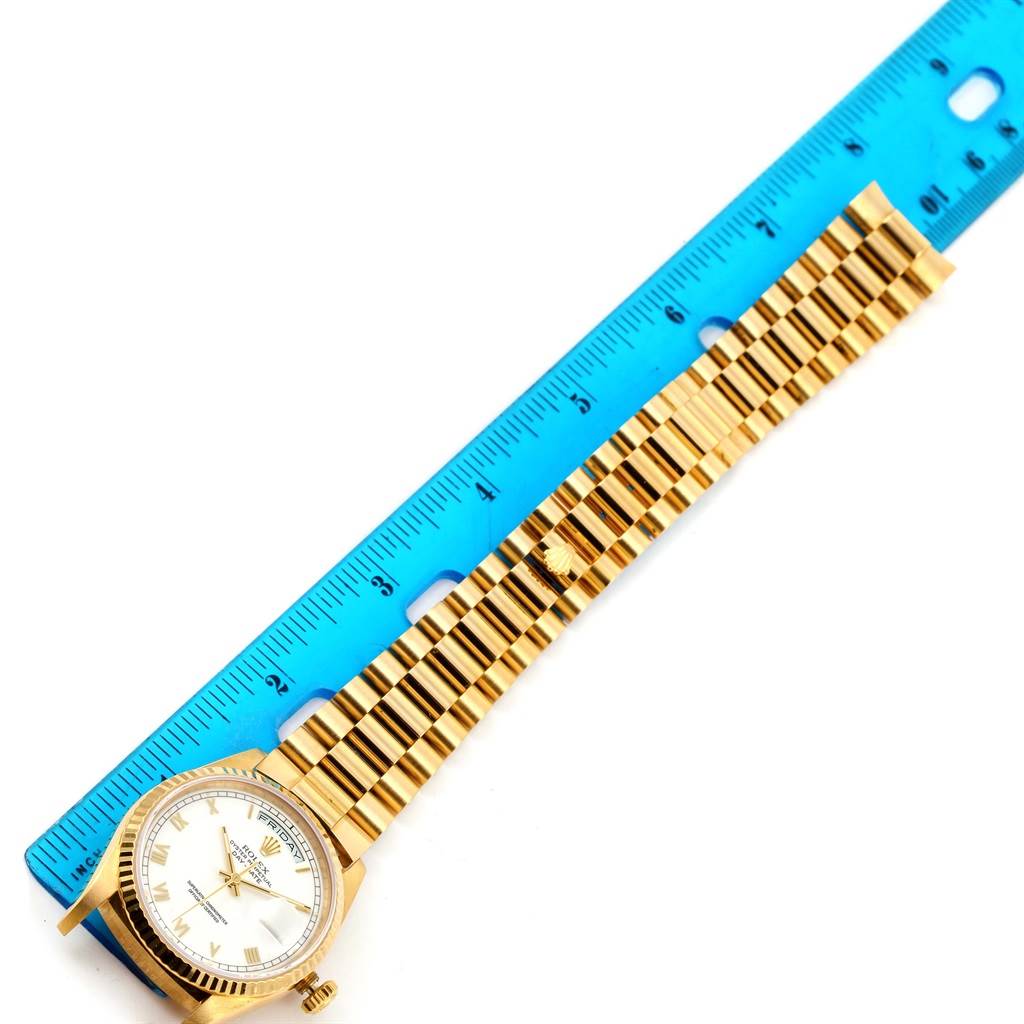 The image shows the face and bracelet of a Rolex President 18238 Men's Yellow Gold White Dial 18238 Men's Yellow Gold White Dial model watch lying next to a blue ruler.
