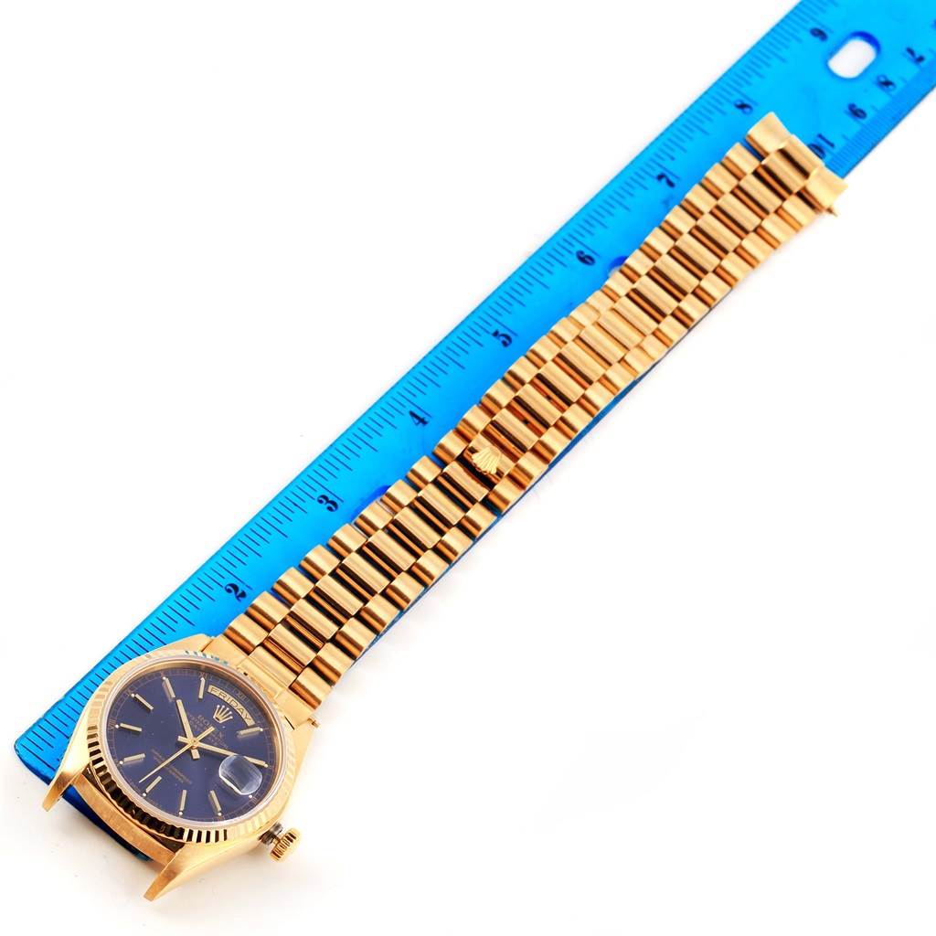 The image shows a Rolex President 18038 Men
s Yellow Gold Blue Dial 18038 Men
s Yellow Gold Blue Dial model watch laying flat, with its strap extended alongside a ruler.