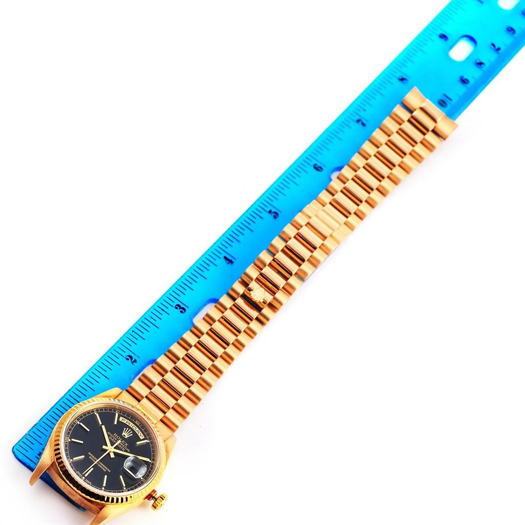 The image shows a Rolex President 18238 Men
s Yellow Gold Black Dial 18238 Men
s Yellow Gold Black Dial watch laid flat next to a blue ruler, displaying the watch face and bracelet.