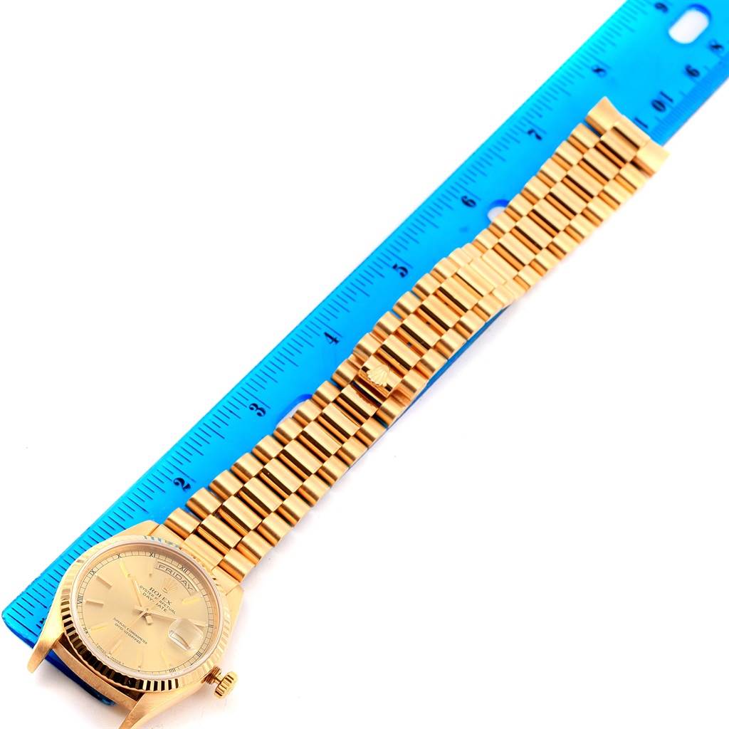 The image shows a top view of a Rolex President 18238 Men
s Yellow Gold Champagne Dial 18238 Men
s Yellow Gold Champagne Dial model watch with its band aligned along a blue ruler.