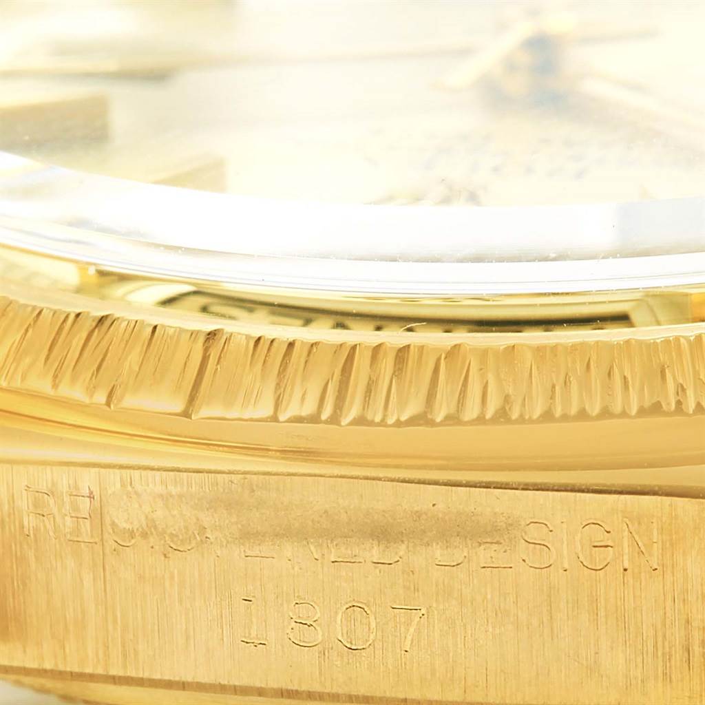 This close-up image of the Rolex President 1807 Men
s Yellow Gold Champagne Dial 1807 Men
s Yellow Gold Champagne Dial model watch shows the fluted bezel and part of the watch case with engraved text.