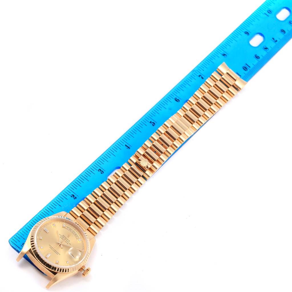 The image shows a Rolex President 18238 Men
s Yellow Gold Champagne Dial 18238 Men
s Yellow Gold Champagne Dial model watch laid flat next to a blue ruler, highlighting its bracelet and face.