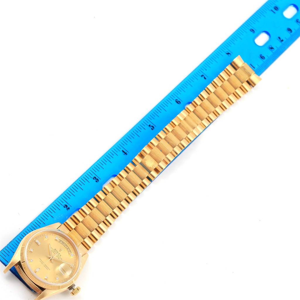 The Rolex President 18078 Men's Yellow Gold Champagne Dial 18078 Men's Yellow Gold Champagne Dial model watch is displayed face up with its gold band fully extended alongside a blue ruler.