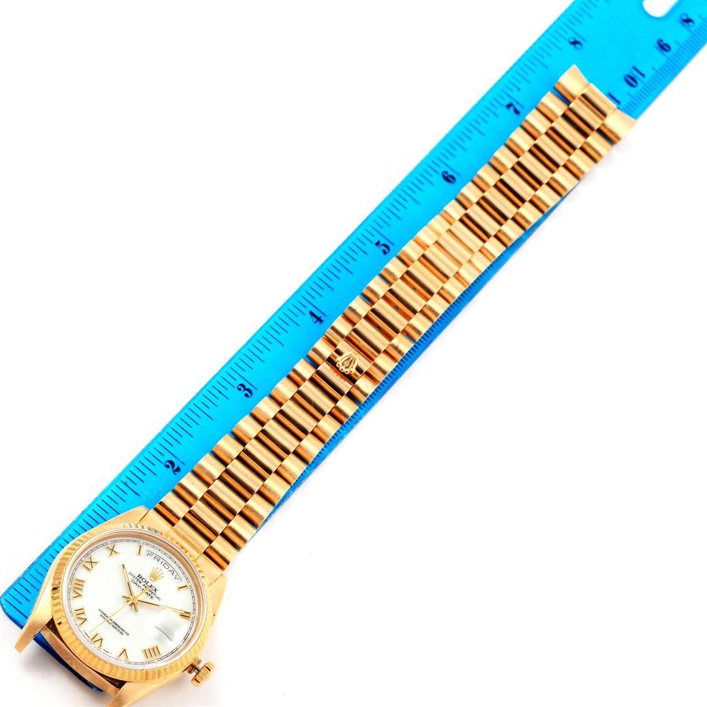 The image shows a Rolex President 18238 Men's Yellow Gold White Dial 18238 Men's Yellow Gold White Dial model watch with its face and full bracelet positioned next to a blue ruler.