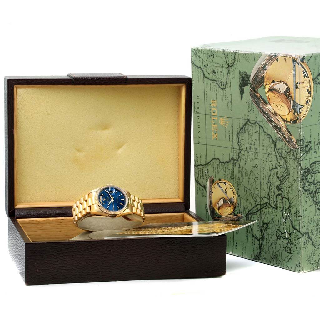 The image shows a Rolex President 18238 Men's Yellow Gold Blue Dial 18238 Men's Yellow Gold Blue Dial model watch with a blue dial, gold band, in an open box with its exterior box beside it.