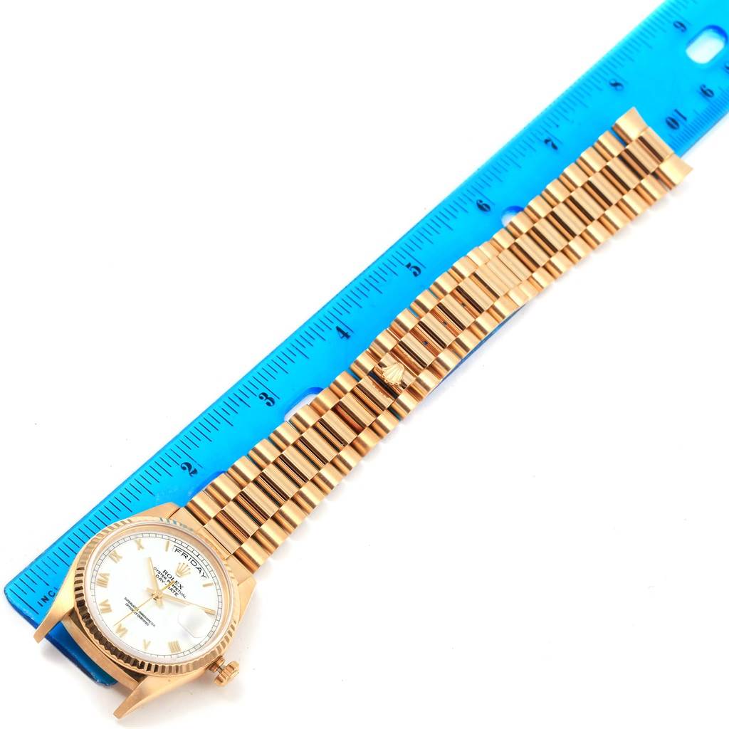 The image shows a President model Rolex watch laid flat with its bracelet aligned along a blue ruler.