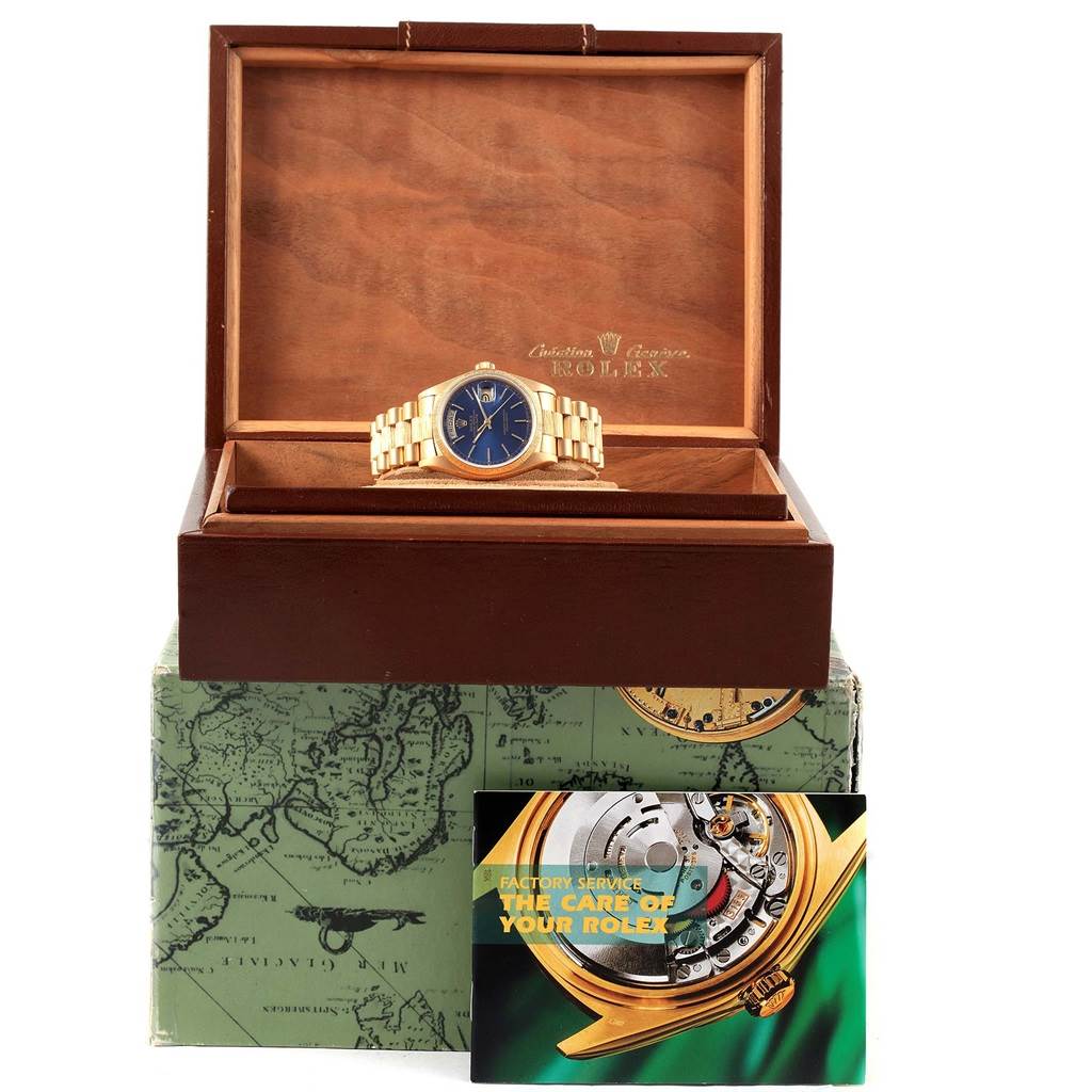 The Rolex President 18078 Men's Yellow Gold Blue Dial 18078 Men's Yellow Gold Blue Dial model watch is shown inside an open wooden box with a booklet and map-themed packaging in view.