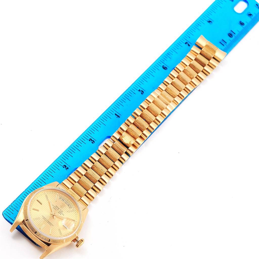 This image shows a gold Rolex President 18248 Men's Yellow Gold Champagne Dial 18248 Men's Yellow Gold Champagne Dial model watch viewed from the top, with the bracelet and case aligned next to a blue ruler.