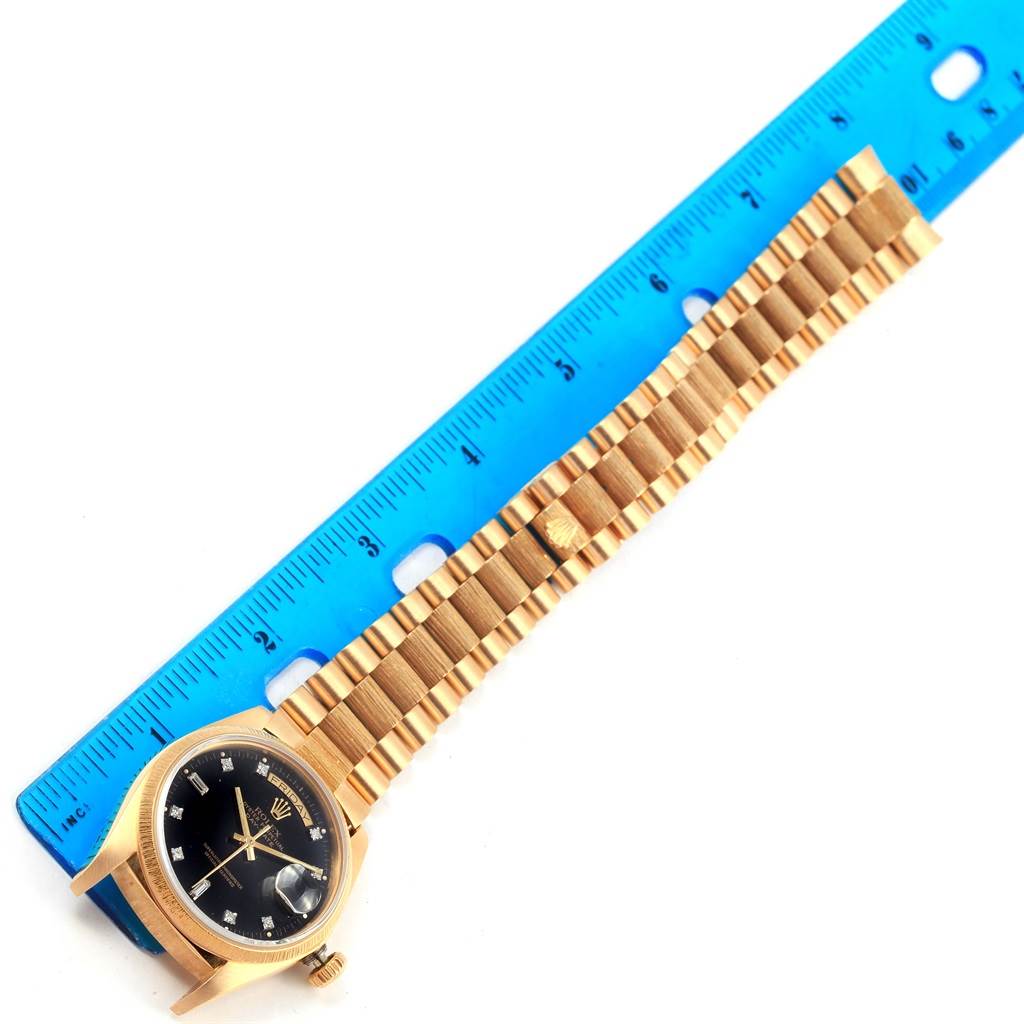 The Rolex President 18078 Men's Yellow Gold Black Dial 18078 Men's Yellow Gold Black Dial model watch is shown from a top-down angle with its face and bracelet visible beside a ruler.