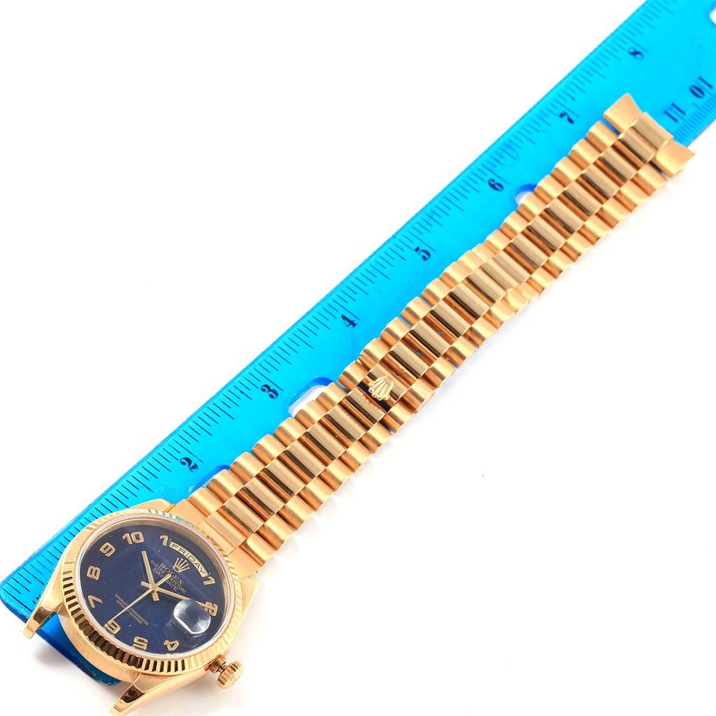 The image shows a Rolex President 118238 Men's Yellow Gold Blue Dial 118238 Men's Yellow Gold Blue Dial model watch laid next to a blue ruler, displaying its gold bracelet and black dial.