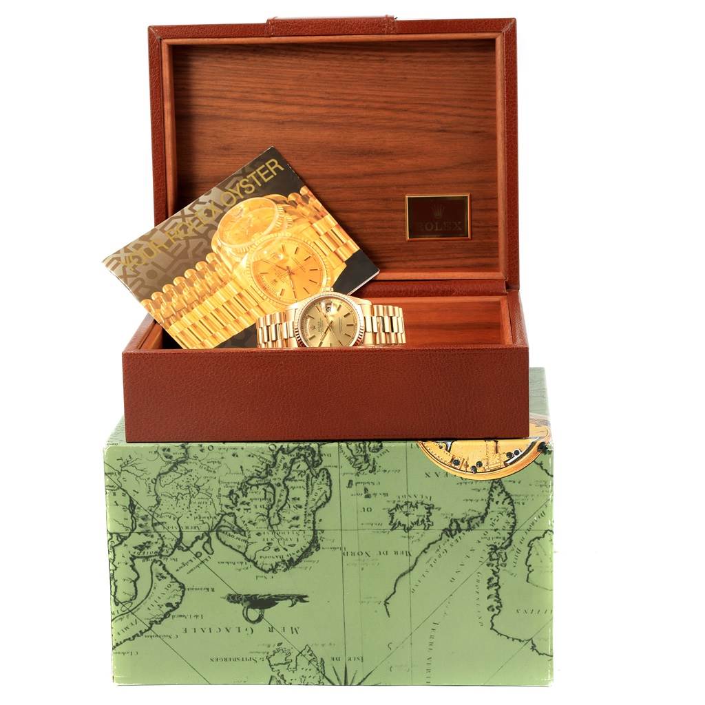 The Rolex President 18238 Men
s Yellow Gold Champagne Dial 18238 Men
s Yellow Gold Champagne Dial model watch is displayed in an open wooden box, accompanied by its brochure and set atop a green map-themed box.