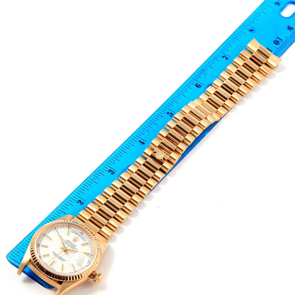 The Rolex President 18238 Men
s Yellow Gold White Dial 18238 Men
s Yellow Gold White Dial model watch is shown lying flat with its gold band against a blue ruler.