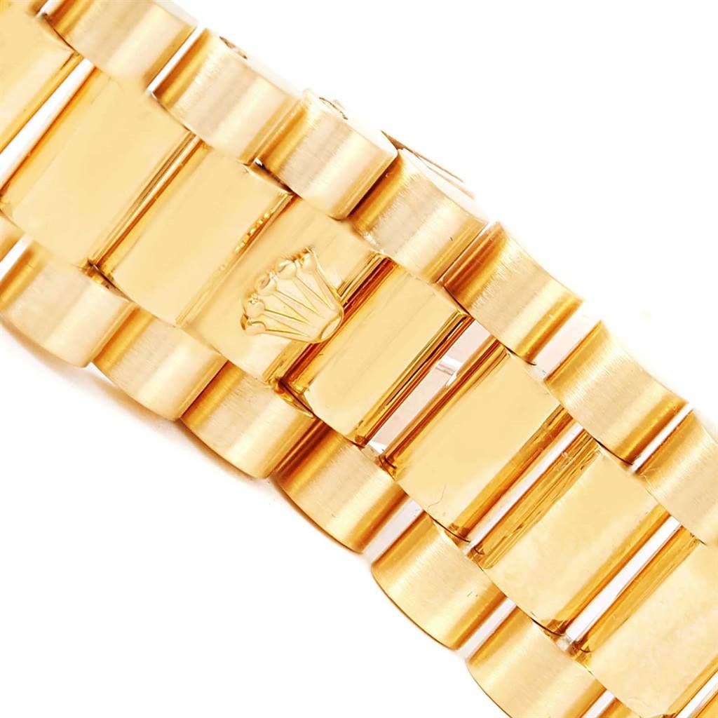 The image shows a close-up of the gold bracelet link from the President model by Rolex, featuring the brand
s crown emblem.