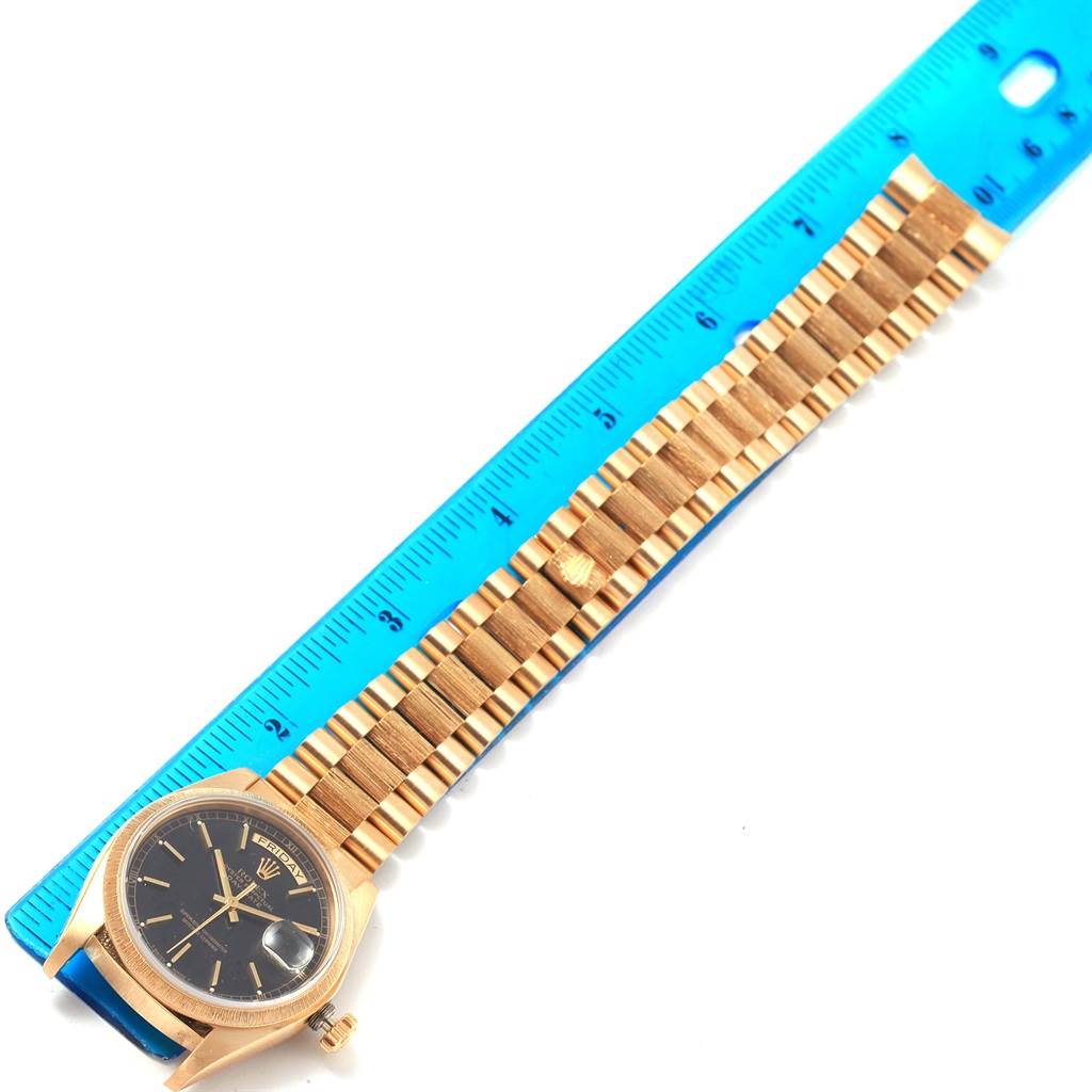 The image shows a President model Rolex watch laid flat next to a blue ruler, highlighting the face and band.