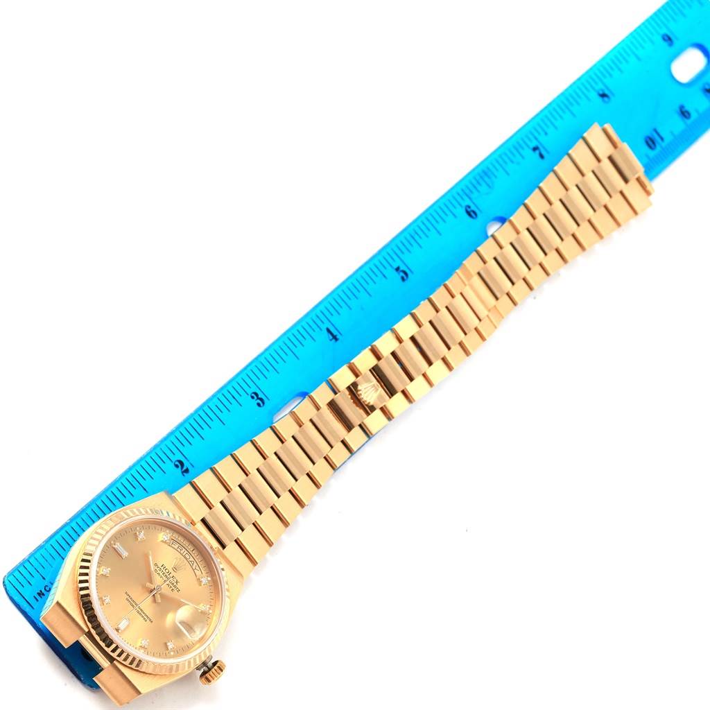 The image shows a Rolex President 19018 Men's Yellow Gold Champagne Dial 19018 Men's Yellow Gold Champagne Dial model watch, with the face and bracelet laid flat against a blue ruler.