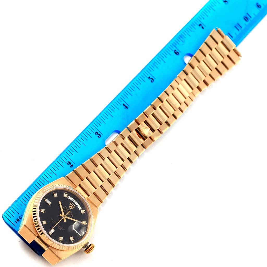 The image shows a Rolex President 19018 Men's Yellow Gold Black Dial 19018 Men's Yellow Gold Black Dial model watch placed beside a blue ruler, with its face and bracelet fully visible.