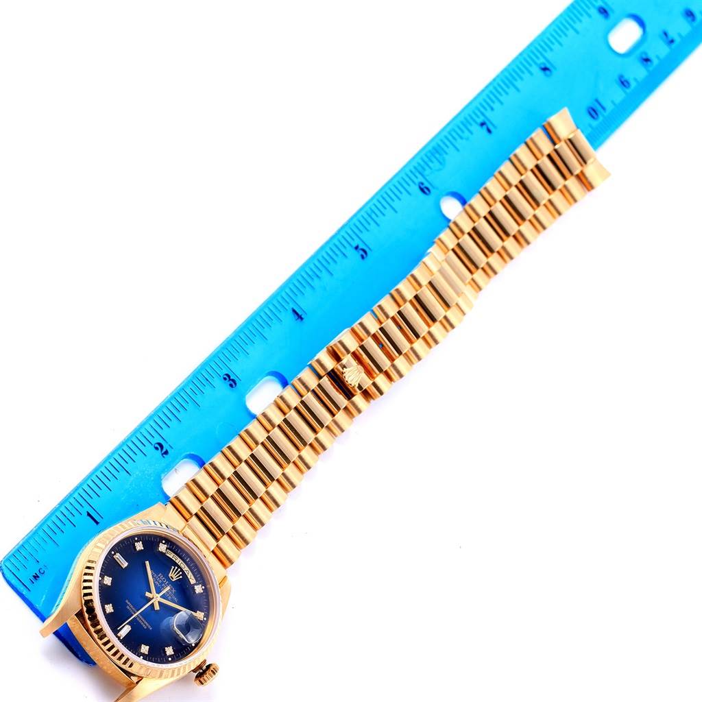 This image shows a Rolex President 18238 Men's Yellow Gold Blue Dial 18238 Men's Yellow Gold Blue Dial model watch laid next to a blue ruler, displaying the watch face and band.