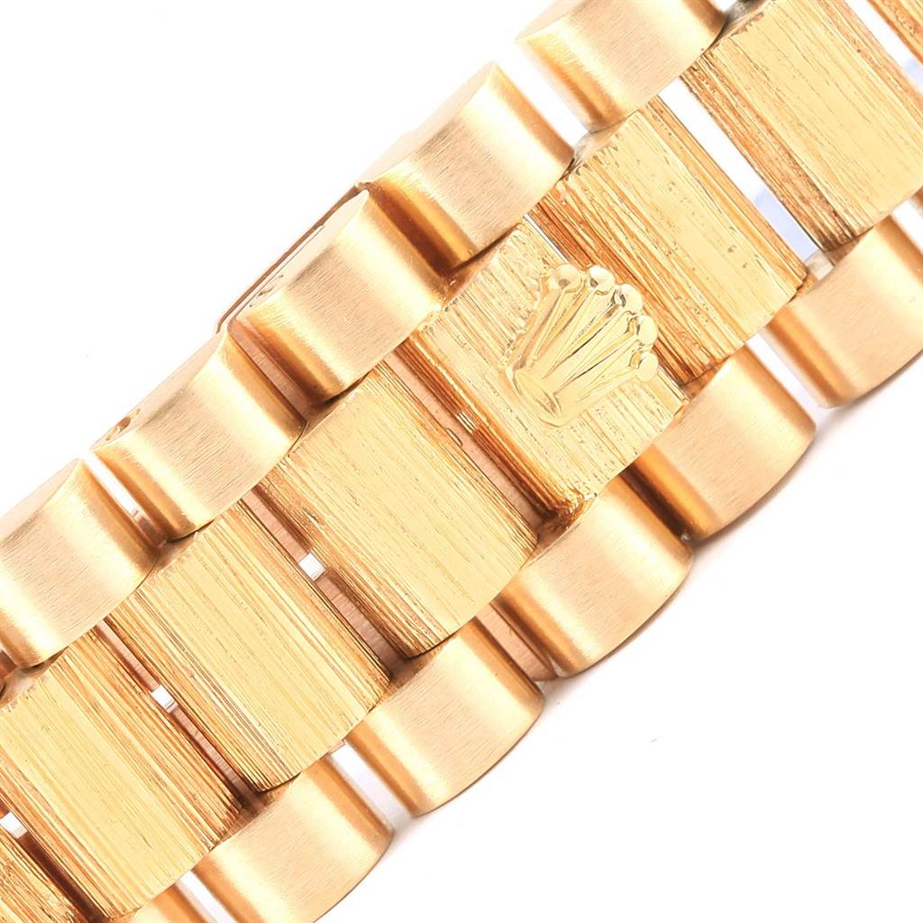 The image shows a close-up of the President bracelet links of a Rolex watch, highlighting the gold finish and the Rolex crown emblem.